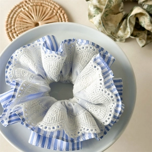 Detailed shot of blue striped cotton scrunchie with white lace trim on a white plate