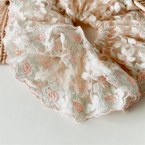 Vue détaillée d'un chouchou en dentelle brodée avec des motifs floraux roses