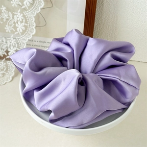 Detail of a purple satin scrunchie with a silk-like texture in a ceramic bowl
