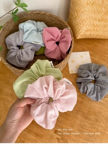 Nahaufnahme bunter karierter Baumwoll-Scrunchies in einem Weidenkorb mit sanfter Ästhetik