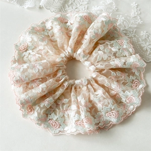 Détail du chouchou en dentelle rose avec broderies florales et bords festonnés