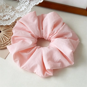 Close-up of light pink fabric scrunchie with soft pleats on a vintage lace background