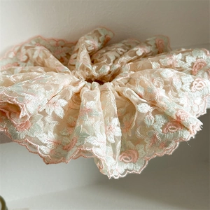 Gros plan sur la broderie florale du chouchou en dentelle beige aux bords festonnés