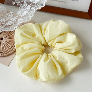 Close-up of pale yellow scrunchie with pleated texture on white lace and rattan mat