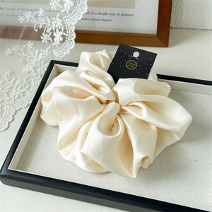 Detailed view of cream satin scrunchie with silky sheen on elegant display tray