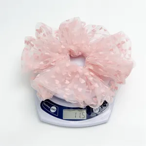 Detail shot showing the lightweight 11.5g pink heart flocking mesh hair scrunchie on a scale