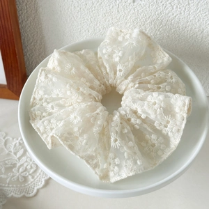 Détail d'un chouchou en dentelle blanc ivoire avec broderie florale et texture en résille