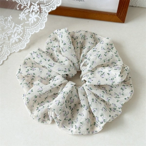 Détail du chouchou en mousseline crème avec motifs floraux violets sur surface en marbre