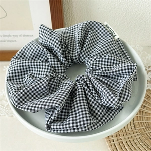 Detailansicht eines schwarz-weißen Gingham-Haargummis mit Logo-Etikett auf einer Schale