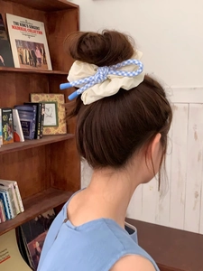 Detail of a creamy yellow oversized scrunchie with a blue and white plaid bow decoration