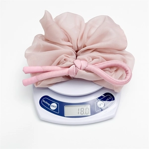 Close-up showing a 18.0g lightweight pink chiffon bow scrunchie on a white scale