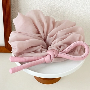 Close-up of pink oversized chiffon scrunchie with soft knot detail on a minimal stand