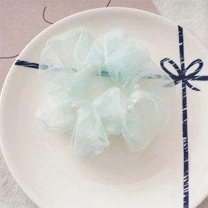 Détail d'un chouchou en organza bleu clair avec perles sur une assiette décorative