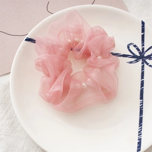 Détail du chouchou en organza rose avec perles blanches sur une assiette décorative