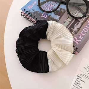 Detail of pleated two-tone scrunchie in black and white on a minimalist white desk
