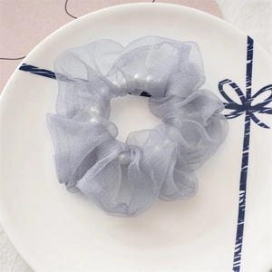 Détail d'un chouchou en organza gris avec perles sur une assiette décorative en céramique
