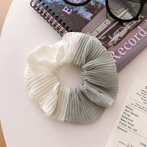 Detailed view of bicolor pleated chiffon scrunchie in beige and sage green on a desk