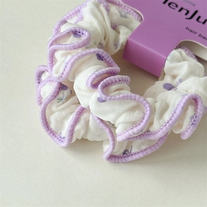 Détail d'un chouchou blanc avec motif floral violet et bordure à volants festonnés