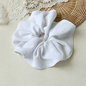 Detail of a large white pleated scrunchie with soft fabric texture and ruffled edges