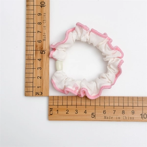Vue détaillée d'un chouchou blanc à bords roses ondulés avec perle mesurant environ 5,5cm