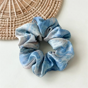 Close-up of blue marble pattern satin scrunchie with rich silk folds and texture
