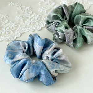 Close-up of elegant blue and green oil-painting satin scrunchies on white lace