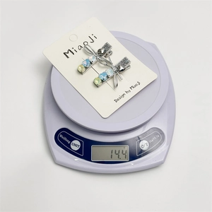 Détail de barrettes bleues à strass en forme de nœud sur une balance indiquant 14,4g