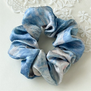 Detail of blue marble print satin hair scrunchie with soft silk texture and lace background