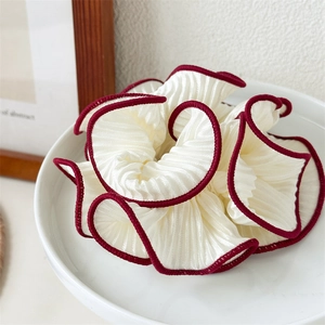 Macro detail of creamy white pleated scrunchie with contrasting deep red stitched edges