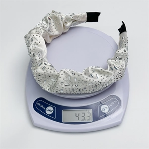 Detailed close-up of a rhinestone headband weighing 43.3g on a scale with pleated fabric
