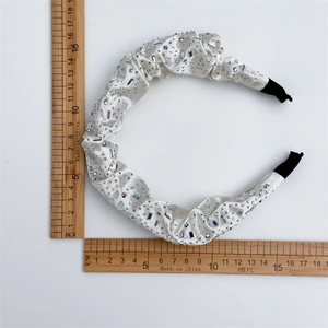 White satin headband with shimmering rhinestones and black protective ends on white background