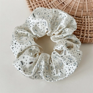 Macro shot of cream satin scrunchie featuring heavy rhinestone embellishments and textures