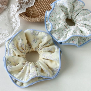 Dettaglio di elastici scrunchie a fiori con bordo blu su un vassoio intrecciato