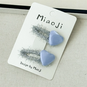 Détail de pinces à cheveux cœur en satin bleu clair avec bordure argentée et strass
