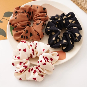 Dettaglio di tre elastici scrunchie con motivo a cuori in caramello, nero e crema