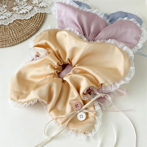 Close-up of satin hair scrunchies with white lace edges and decorative vintage buttons