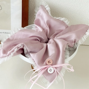 Detail of soft pink satin scrunchie featuring white lace edges and decorative buttons