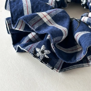 Detailed macro view of the navy blue plaid fabric scrunchie with white flower embroidery