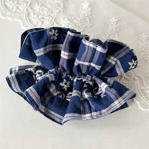 Detail of blue plaid hair scrunchie with floral embroidery on white lace background