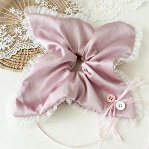 Detailed macro view of pink satin scrunchie with lace edges and decorative buttons