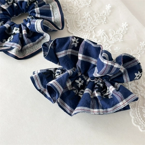 Detailed close-up of blue plaid scrunchies with white floral embroidery and lace edges