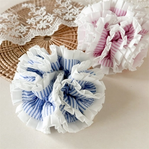 Close-up of blue and pink striped scrunchies with white pleated lace edges on a woven mat