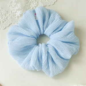 Detailed macro view of light blue pleated fabric scrunchie with handmade woven label