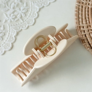 Close-up of beige glossy claw clip with golden spring on a lace background