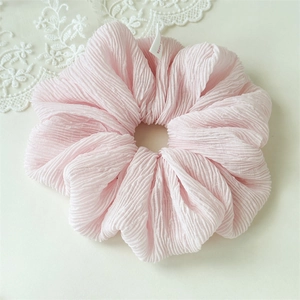 Close-up of a pink puffy fabric scrunchie with a handmade label and lace detail