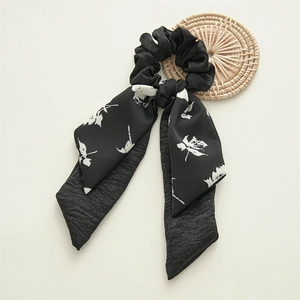 Detail of black scrunchie with white floral pattern and long ribbons on woven mat