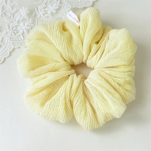 Detail of light yellow pleated scrunchie with hand made heart label on fabric surface