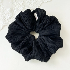 Close-up of black pleated fabric hair scrunchie with detailed texture and white label