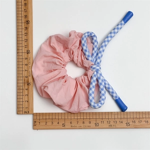 Détail d'un chouchou rose plissé avec ruban à carreaux bleus et règle pour les dimensions