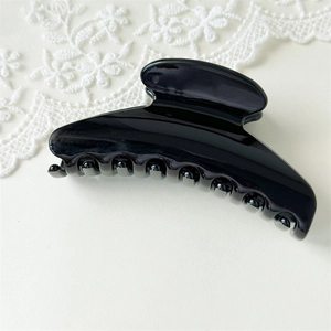 Detail of elegant glossy black fan-shaped hair claw clip on a soft floral lace background